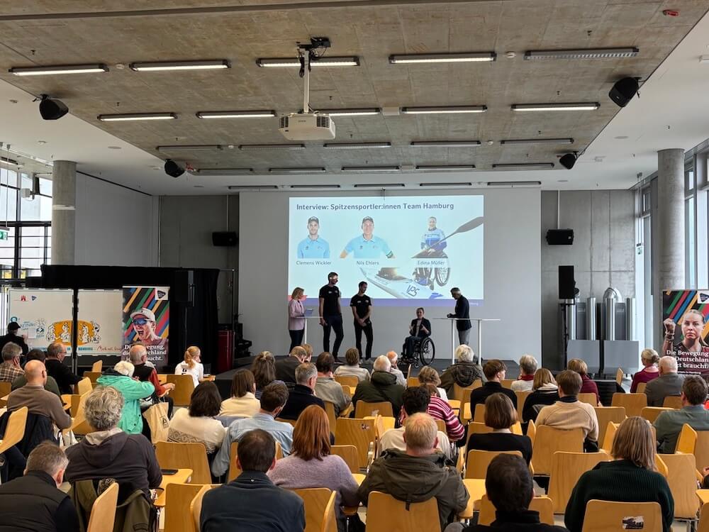 Drei Olympioniken werden auf der Bühne von Moderatoren interviewt