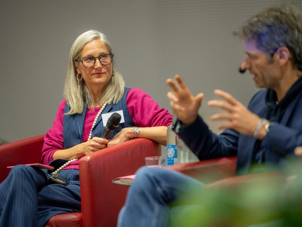 isabell-koester-moderation-keynotes-workshops-credit-muhme-photography Isabell Köster sitzt mit Mikrofon auf der Bühne und hört einer anderen Person zu